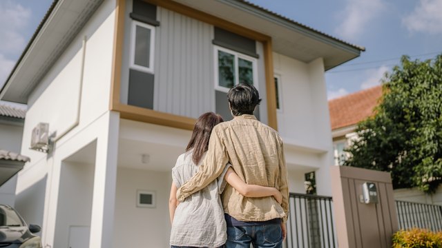 A couple stand arm in arm looking up at a newly built two-storey house